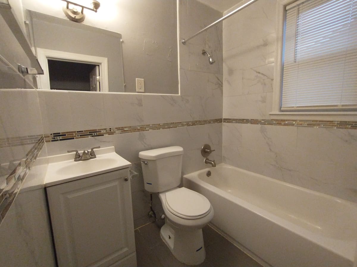 Finished unit bathroom with marble-pattern tile tub surround, mosaic accent band, new vanity, fixtures and lighting.