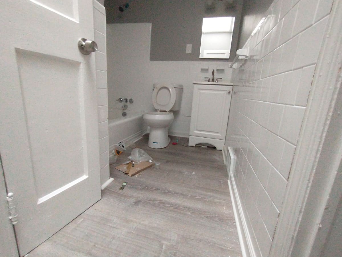 Unit bathroom mid-renovation: new tile, tub and vanity set in place, with installation debris and packaging still on the floor.