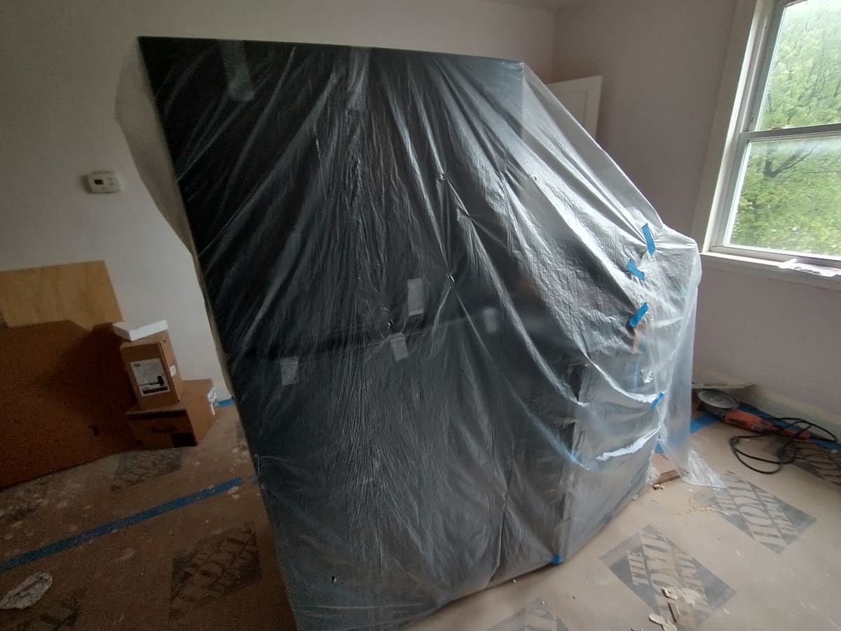 A vacant room sealed with taped plastic sheeting and floor protection during drywall repair.