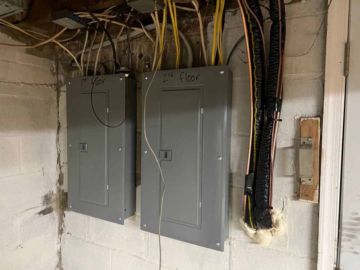 Two replacement electrical panels hand-labelled first floor and second floor, mounted on a basement block wall with new feeder wiring above.