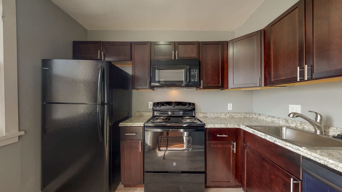 Finished unit kitchen with dark wood cabinetry, granite countertops, and new range, microwave and refrigerator.