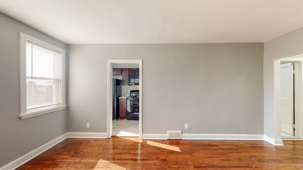 Vacant finished living room with refinished hardwood floors, repainted walls, and an opening through to the kitchen.